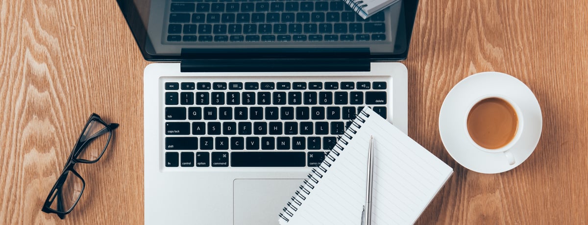 Overhead shot of a laptop, glasses, and notepad