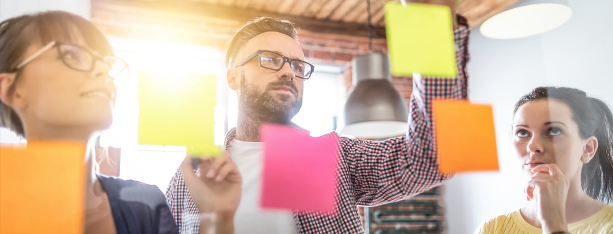 Employees look at wall of post it notes