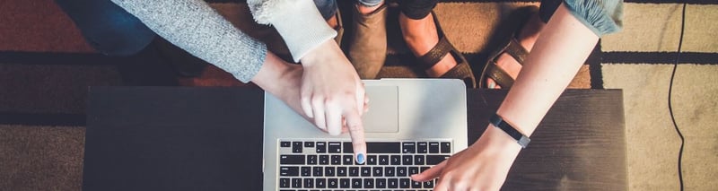 Several hands working on a laptop while coworkers are sharing ideas 