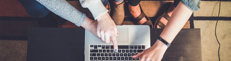 Several hands working on a laptop while coworkers are sharing ideas