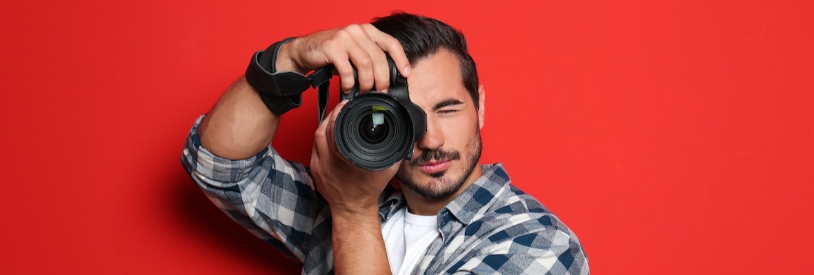 Young professional photographer taking picture on red background