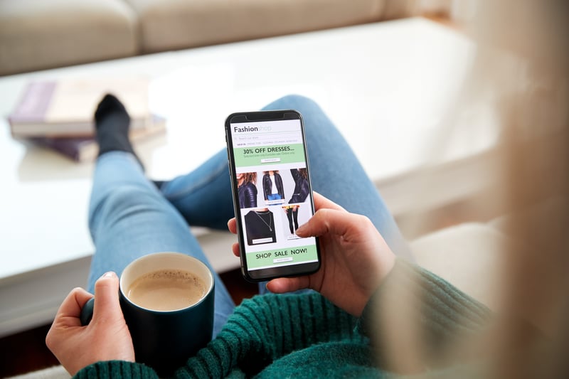 Person holding a coffee mug and browsing an apparel Shopify landing page on their phone