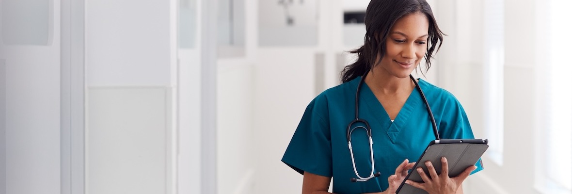 Female Doctor Wearing Scrubs In Hospital Corridor Using Digital Tablet