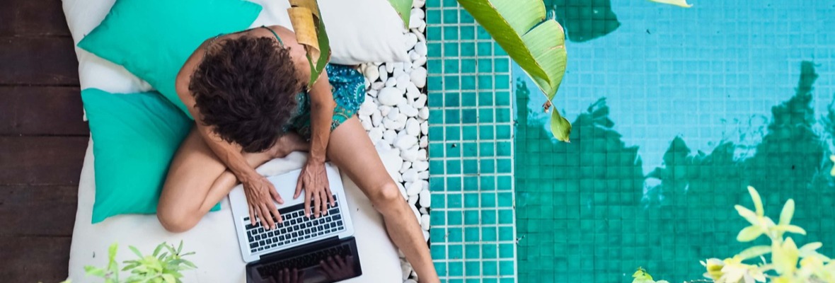 Woman working on her laptop wearing a bathing suit next to a swimming pool