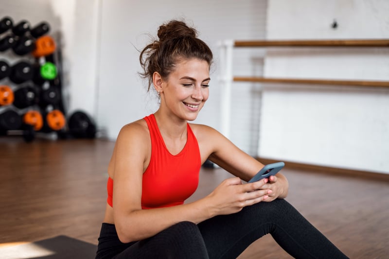 Woman in gym opening a personalized email from her fitness center on her smartphone