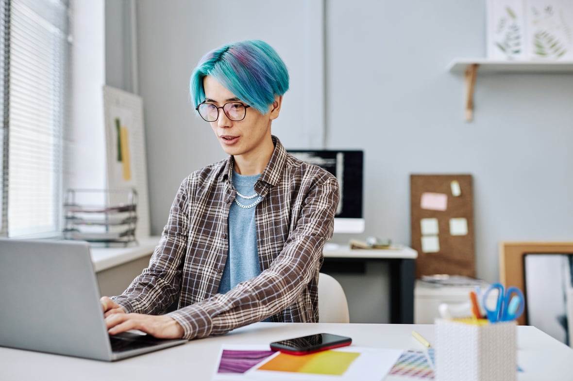 Person with blue hair working on laptop at their desk