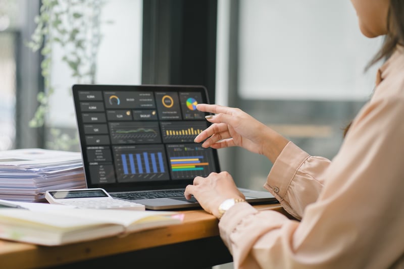 A close up image of two hands working on a desk and one pointing at a screen that has metrics on it