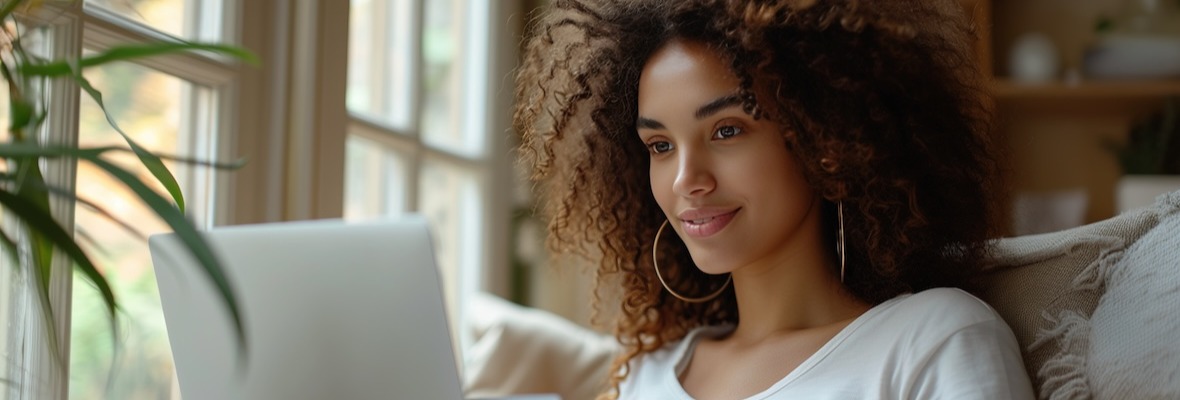 A curly woman sits at a laptop and makes purchases online at home