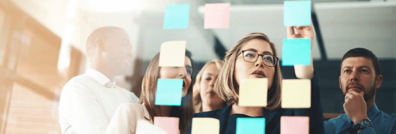 A group of co-workers review post-it notes on a whiteboard. 