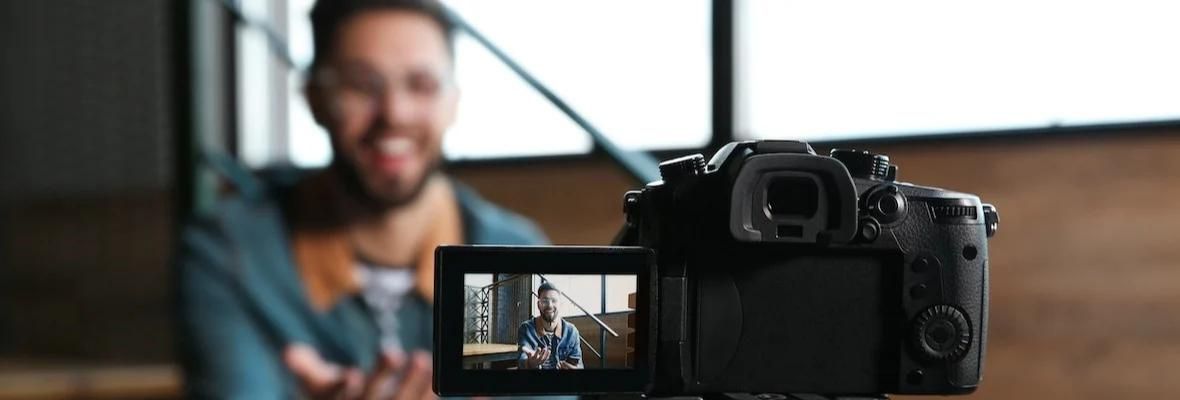 Young blogger recording video indoors, focus on camera screen.