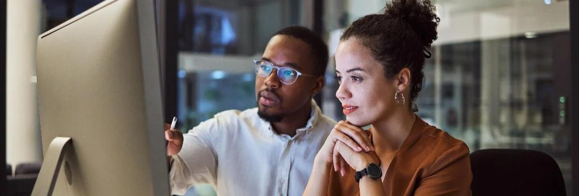 Two coworkers look at a computer screen and analyze data together. 