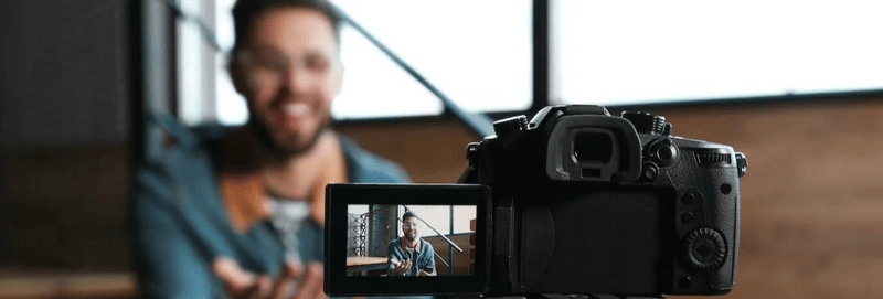 Young blogger recording video indoors, focus on camera screen.