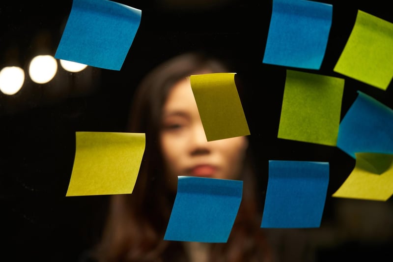 Close up image of a transparent board with post its and a woman behind it looking into them
