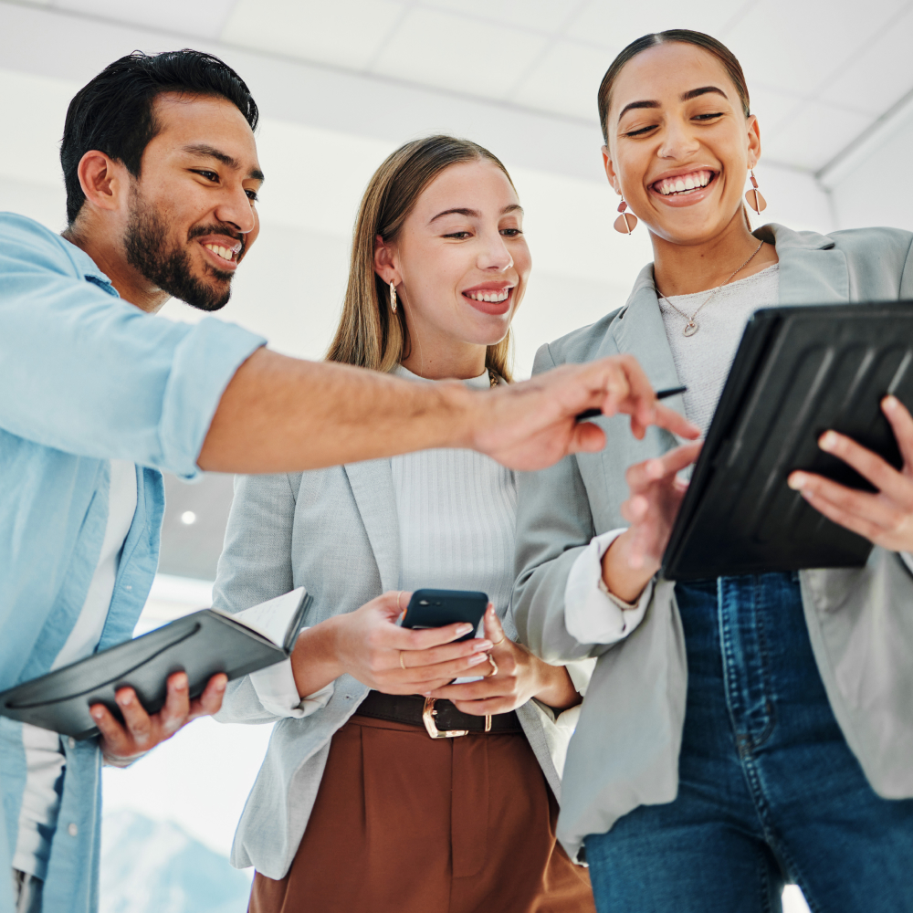 Two women and a man looking at a tablet while smiling