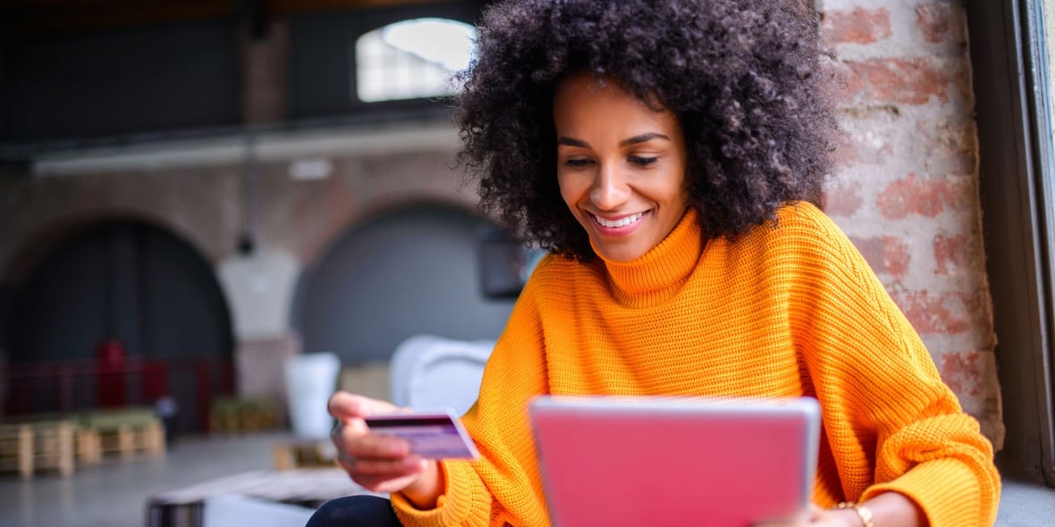 Woman looking at a computer while holding a credit card on her hand