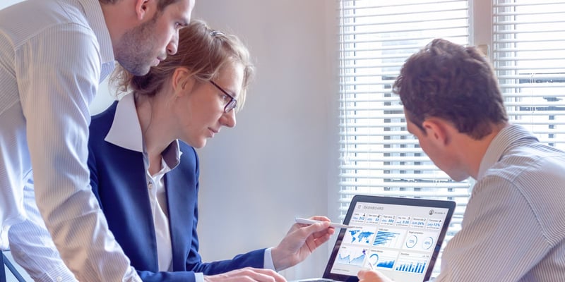 Three marketers looking at a laptop screen with a metrics dashboard in it