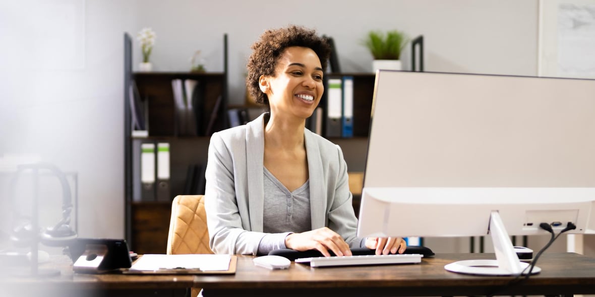 Short haired woman working at a desk and smiling at her desktop