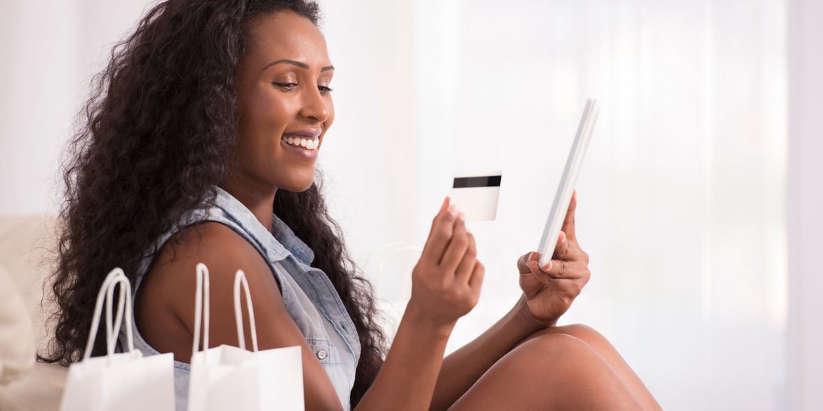 Woman looking at her credit card while smiling and holding a tablet on her hands