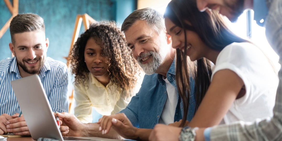 A group of marketers discussing strategies together while looking at a laptop