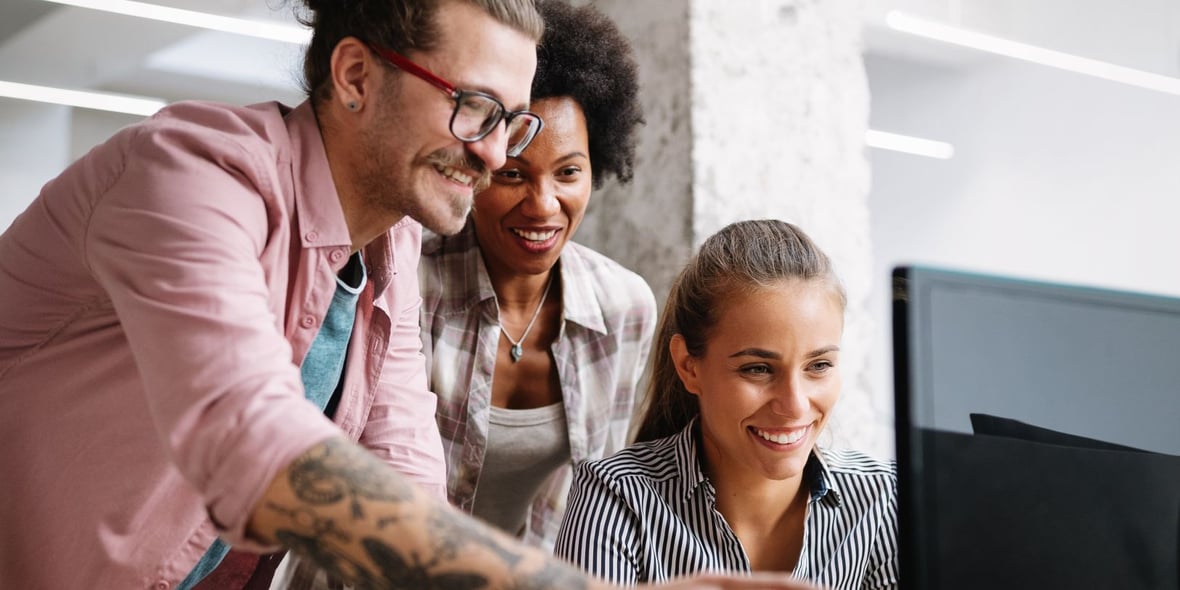 Three marketers working and looking at a computer while smiling