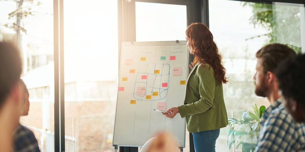 Woman in front of white board showing a strategy to her team