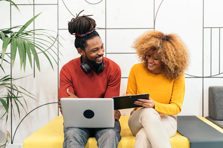 two people smiling at each other and working on a laptop