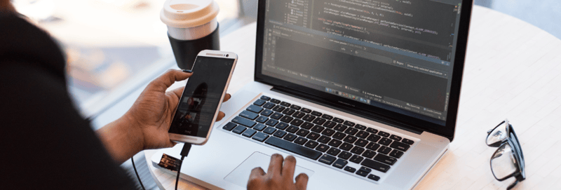 Close up image of two hands working on a laptop while holding a smartphone