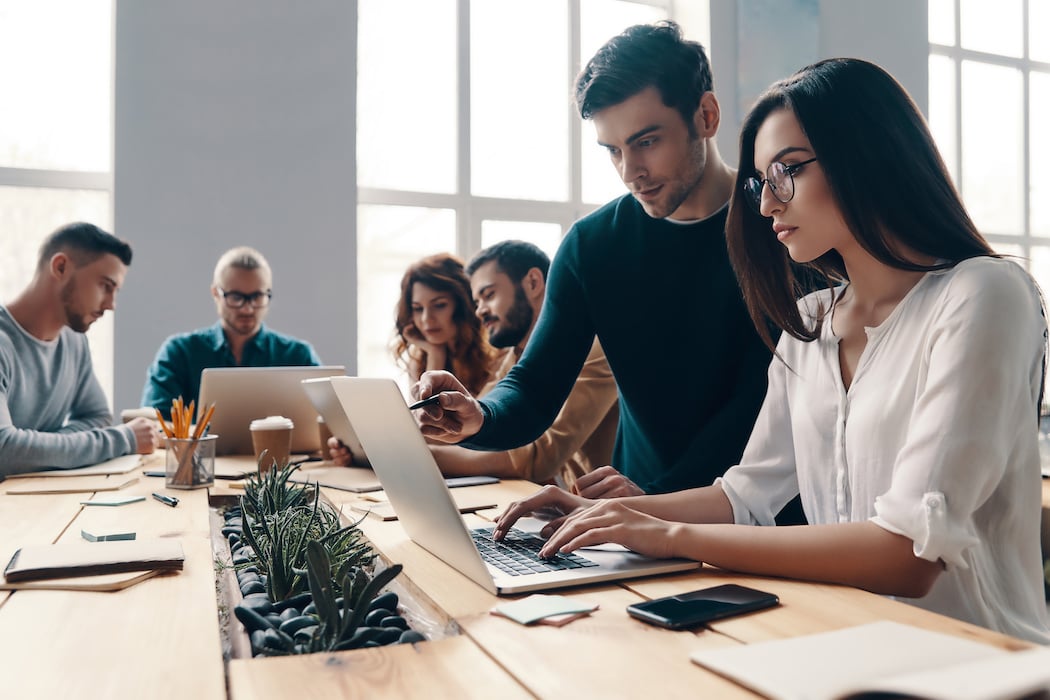 Team of marketers use ChatGPT prompts for marketing at laptops in a well-lit office around a solid wood table.