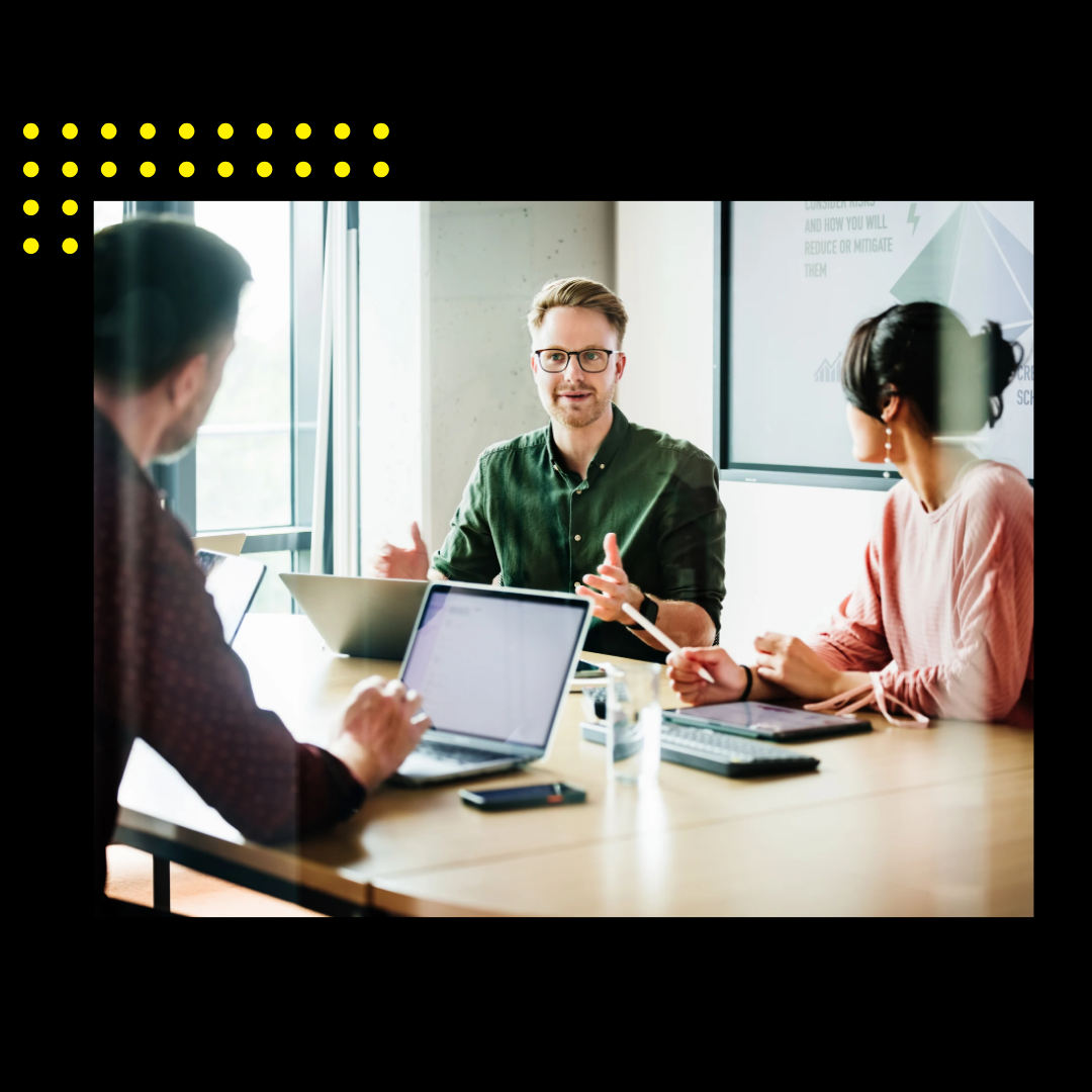 A focused team leader is addressing colleagues in a meeting, with a presentation displayed in the background, capturing a moment of active corporate engagement