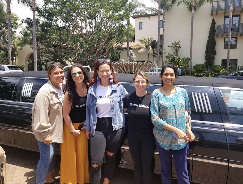 Five people smiling together in front of a limousine, with several of them wearing SmartBug Media t-shirts