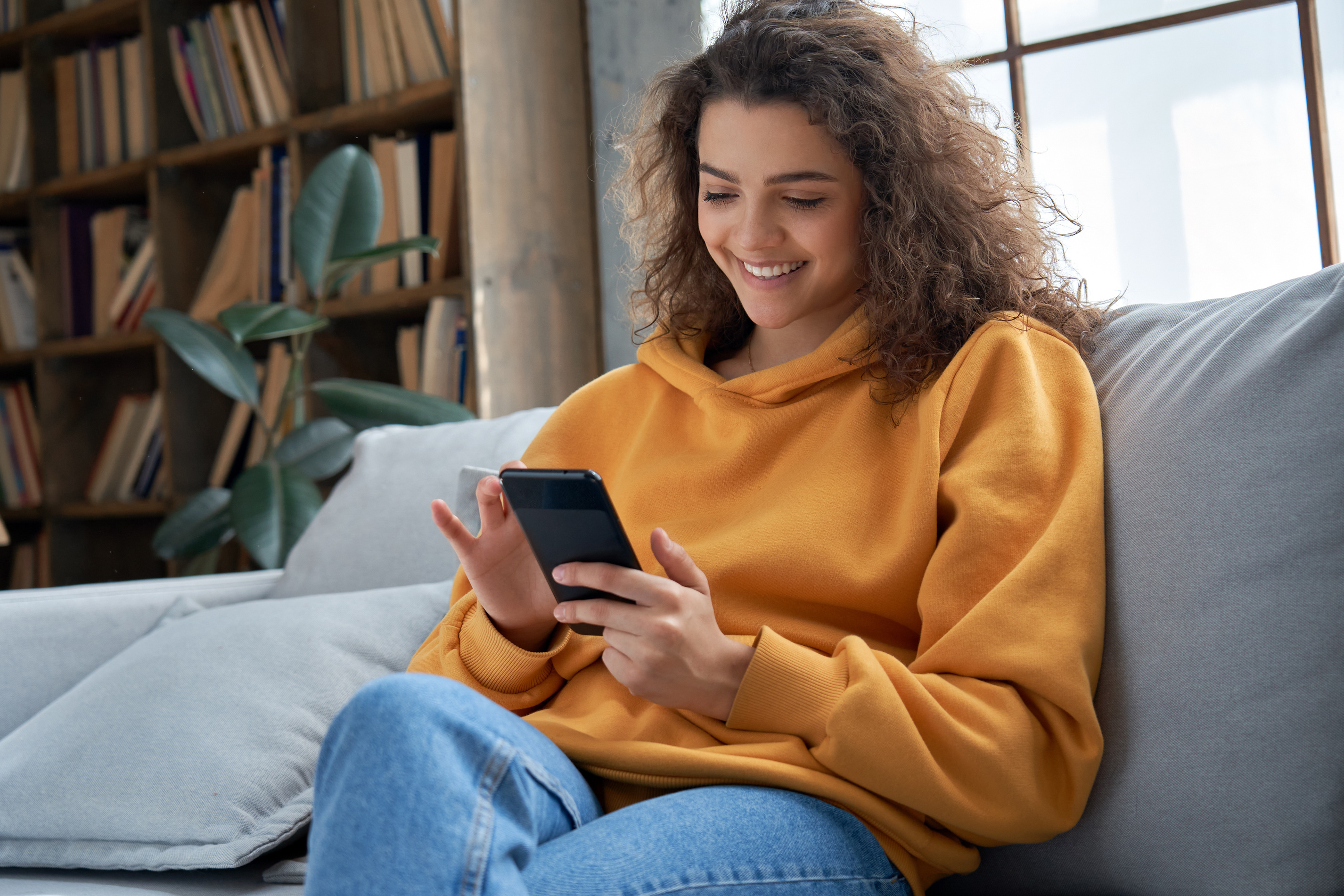 Woman sitting on a couch smiling and scrolling through her phone